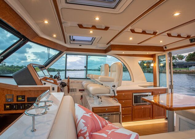 Salon of the Back Cove 39O featuring twin helm seats, wood cabinetry, galley with microwave, and a large wraparound windshield