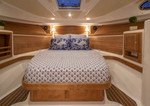 A forward stateroom with a centered island berth, wood accents, and patterned blue bedding in the Back Cove 34O