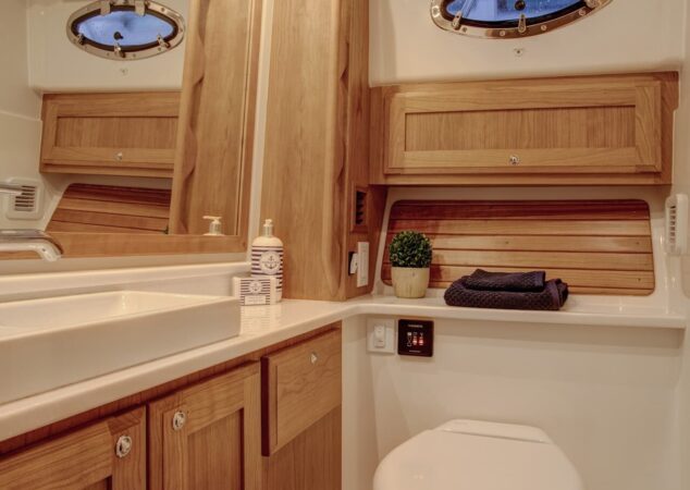 The enclosed head aboard the Back Cove 34O, featuring a toilet, countertop, cabinetry, and oval porthole windows