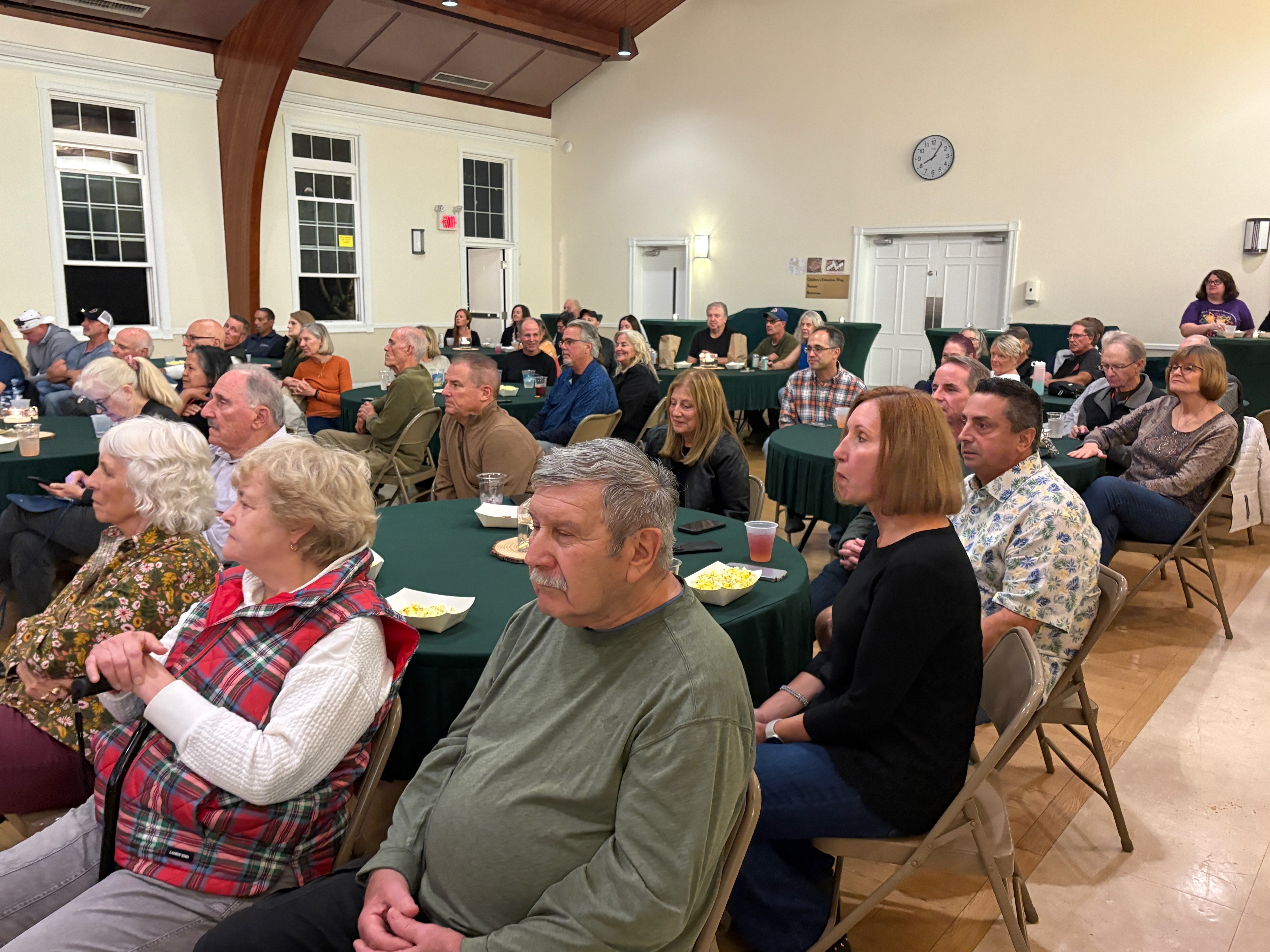 A full audience seated at green-draped tables enjoying the concert