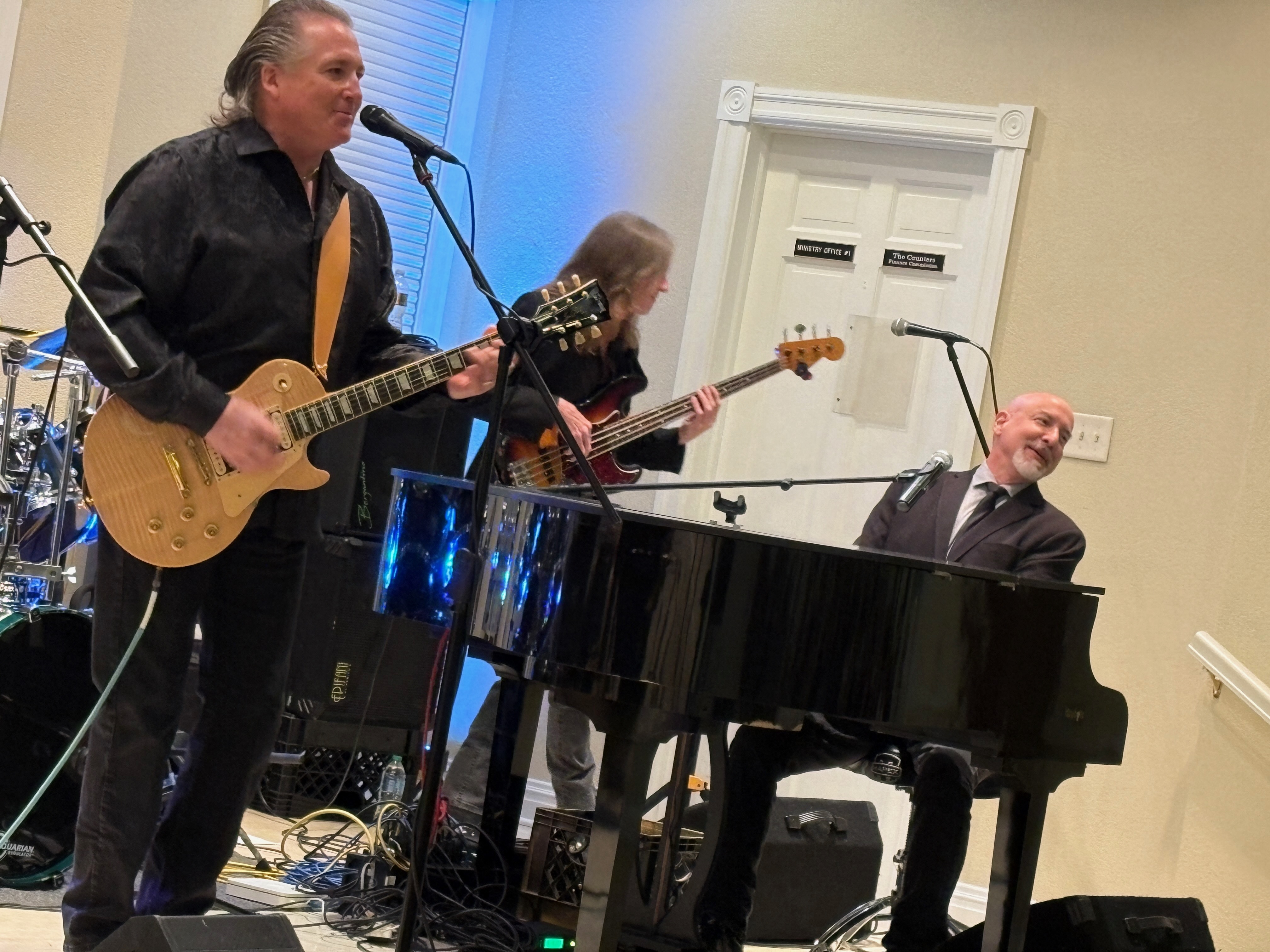 The guitarist, bassist, and pianist smiling mid-song