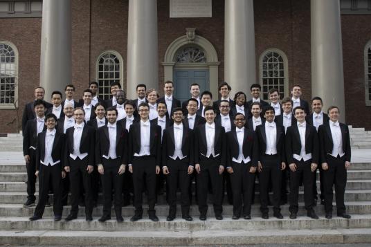 A photograph shows a group of male students in formal attire standing together on steps in front of a building.