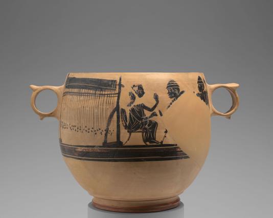 A bowl-shaped vessel made of light brown clay shows a painting in dark brown and black of a person seated beside a large loom.
