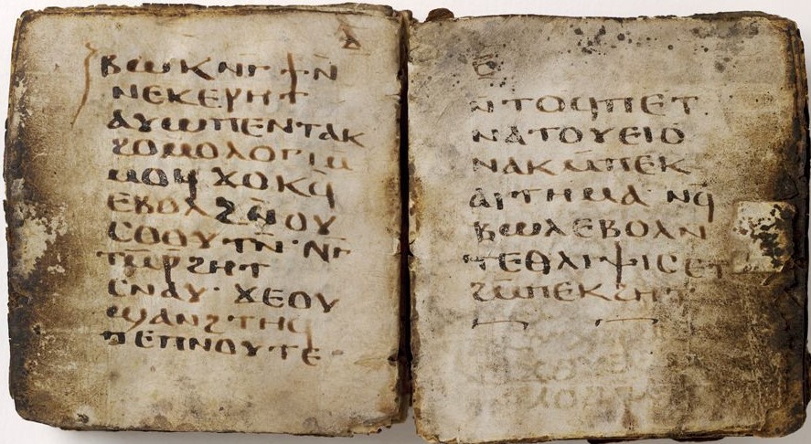 An open book reveals rows of Coptic letters, handwritten in dark brown ink. The pages are darkened, and the frail edges are irregular.