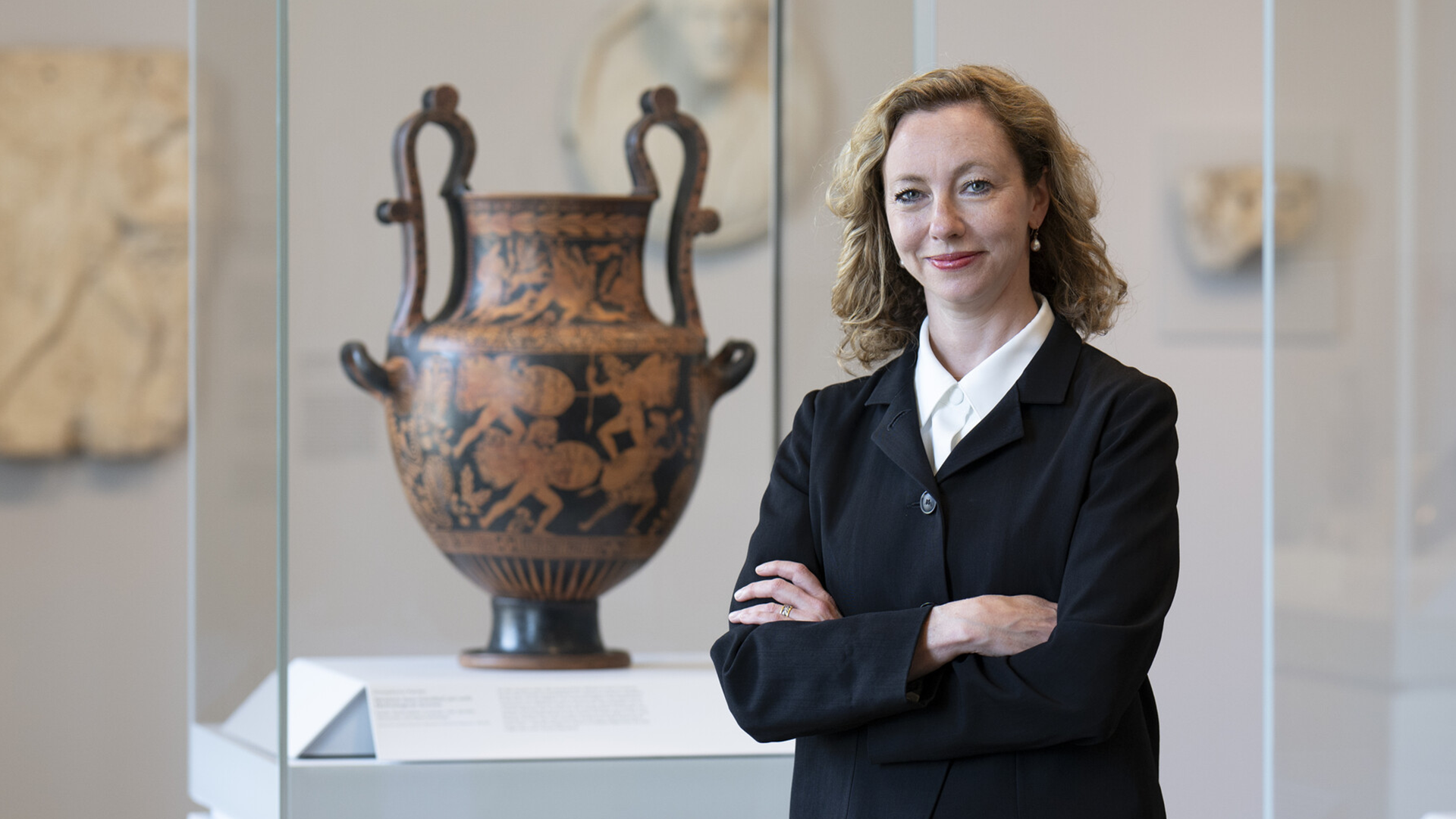 A woman stands with her arms crossed in front of a large clay vessel in a gallery.