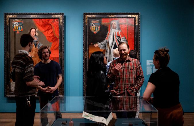 Vistors gather in front of large portraits in a blue walled gallery.