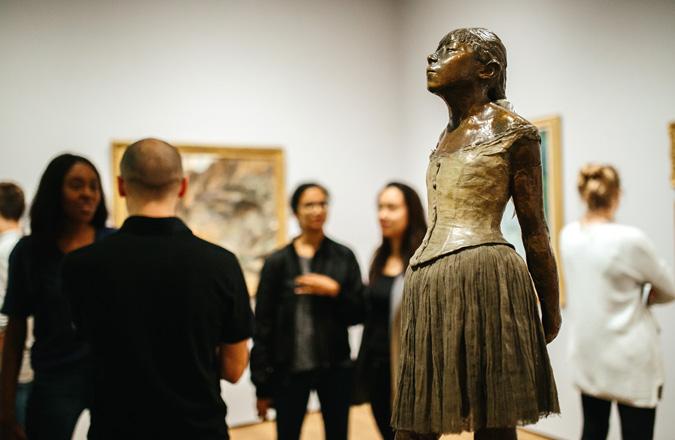 A bronze statue of a young girl with museums visitors gathering behind it.