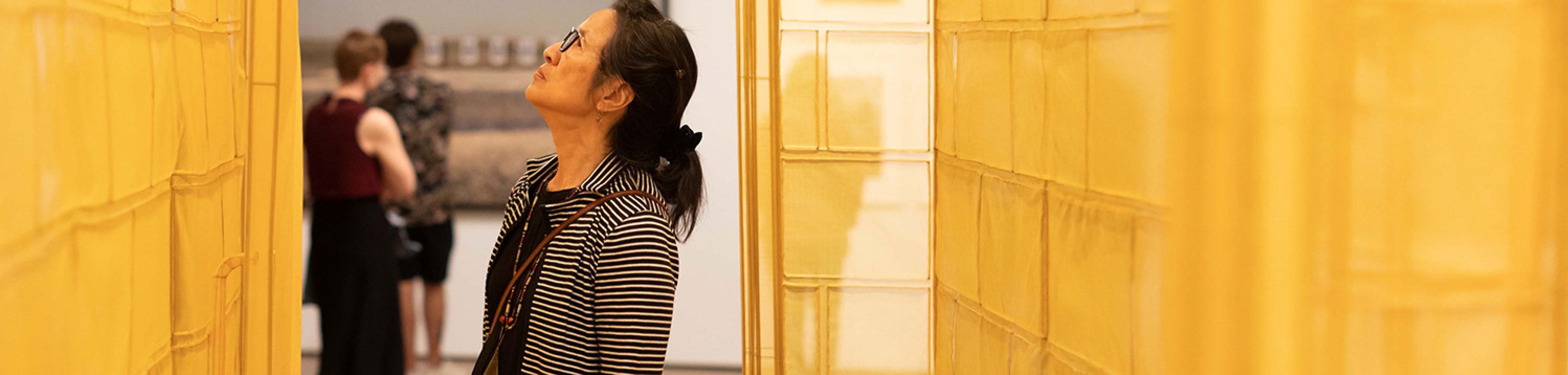A woman looks up while surrounded by the gold, semi-translucent material of an art installation.