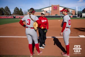 Nebraska Cornhusker head coach Rhode Revelle works with Bella Bacon (3) and Mckinley Malecha(00) warming up for Minnesota during a college softball game Friday, March 21, 2025 in Lincoln, Nebraska. Photo by John S. Peterson.