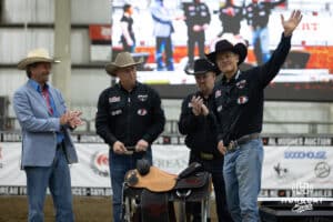 John Cook waves to the fans after Travis Schauda described the saddle presented by Greg Olson, in the blue jacket, Owner of Vitalix Inc to John Cook during the John Cook Roping Classic on Sunday, April 13, 2025 in Lincoln, Nebraska. Photo by John S. Peterson.