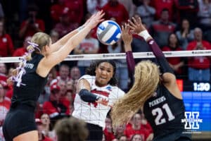 Nebraska Cornhusker middle blocker Manaia Ogbechie (14) spikes the ball between Texas A&M Aggie outside hitter Emily Hellmuth (4) and middle blocker Morgan Perkins (21) in the fourth set during the NCAA Volleyball Regional on Sunday, Dec. 14, 2025, in Lincoln, Nebraska. Photo by John S. Peterson.