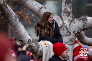 Nebraska Cornhusker fan in a tree listens to the Cornhusker Marching Band warm up before heading over to the stadium for a college football game against the Iowa Hawkeyes on Friday, Nov. 28, 2025, in Lincoln, Nebraska. Photo by John S. Peterson.