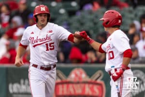 Nebraska Cornhusker Dylan Carey (15) fist bumps Drew Grego after scoring a run against the Kansas State Wildcats in the first inning during a college baseball game at Haymarket Park on Tuesday, April 28, 2026, in Lincoln, Neb. Photo by John S. Peterson.