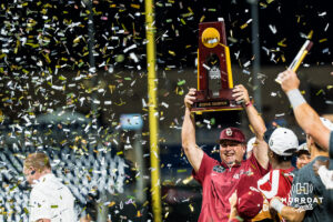 Oklahoma Sooners head coach Skip Johnson holds up the trophy after a CWS game on June 22, 2026, in Omaha, Nebraska. Photo by Brandon Tiedemann.