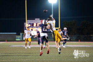 Two boys football players compete during a game on an outdoor field.