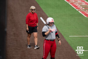 Head coach Rhonda Revelle walks along the base path behind a Nebraska batter in a college softball game.