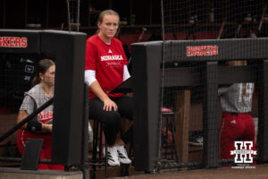 Assistant coach Jordy Frahm watches from the Nebraska dugout in a college softball game.