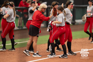 Head coach Rhonda Revelle high-fives Faith Aragon as Nebraska players come off the field in a college softball game.