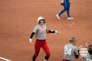 Jesse Farrell celebrates with Cali Bentz and Nebraska players after scoring a run in a college softball game.