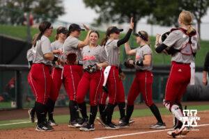 Faith Aragon smiles as Nebraska players exchange high-fives at the end of an inning in a college softball game.