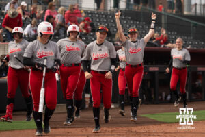 A Nebraska player raises her arms as Nebraska players run out of the dugout in a college softball game.
