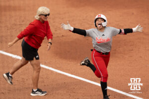 Natalia Hill celebrates as she rounds the bases past a Nebraska coach in a college softball game.