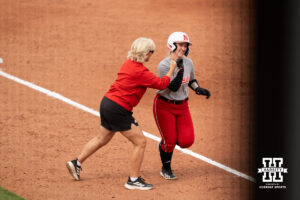 Samantha Bolding bumps fists with head coach Rhonda Revelle while rounding third base in a college softball game.