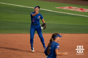 Timber Hensley points and shouts after a play as Kansas players leave the field in a college softball game.