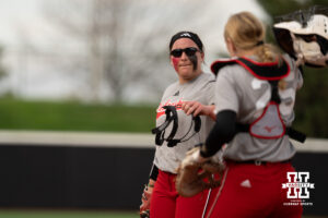 Alexis Jensen hands a face mask to a Nebraska player in a college softball game.