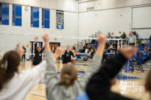 Erin Cramer and Fallyn O'Connell celebrate a point as fans in the stands cheer in a high school volleyball match.
