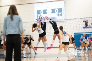 Lyric Judson attacks the ball as Erin Cramer and Taylor McLeay go up for a block in a high school volleyball match.