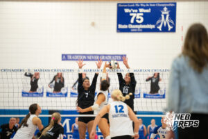 A Papillion-LaVista South player attacks the ball as Trinity Rocha and Fallyn O'Connell go up for a block in a high school volleyball match.