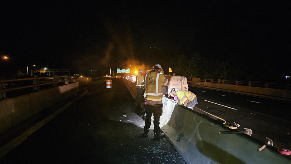 Workers cutting bituminous concrete behind temporary barrier