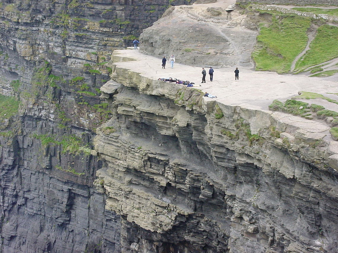 Carefully enjoying the cliffside view These people exercise extreme caution and with good reason. If you slip here, you fall about 214 meters down.This picture is taken at the Cliffs of Moher, Ireland Cliffs of Moher,Europe,Ireland