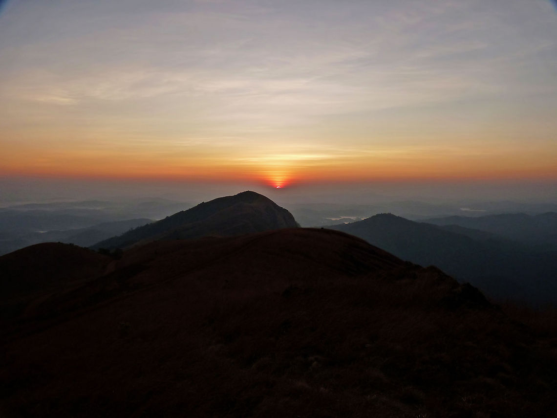 Being at the right place at the right time &quot;Sunrise point&quot;, Kodachadri, Western Ghats, Shimoga - It was a rough night after a tiresome trek for a couple of new trekkers in the group, and the next morning we were to see the sunrise that was supposedly an awesome scene to fill our eyes with.<br />
<br />
Excitement is a hard feeling to come by when your legs are singing songs of pain from the previous day&#039;s trek. This being a reason, a few guys got up later than we were suppose to be up by. Luckily, it wasn&#039;t too late, as the plan was to go to a near by hill (around 10 minutes away) on a Jeep.<br />
<br />
A person drove our group to the sunrise point on a crude road, and it was still quite dark when we reached there. We rested for 10 - 15 minutes before we started to see the sky illuminate with shades of blue, and the land - hazy with orange tint. We were all prepared to be mesmerized while keeping our fingers crossed for the sky to be clear during the moment we were all waiting for. It was the moment of truth, and within a minute, we saw the sky change colors like a Chameleon, while the ball of fire slowly started to emerge in the backdrop. Till date, it is one of the most beautiful sunrises we ever got to witness!<br />
<br />
In a few minutes, the Sun was above the horizon and the fog started to clear out, revealing a series of landscapes for as far as our vision could reach. Geotagged,India,colorful,dawn,india,karnataka,kodachadri,sunrise,western ghats