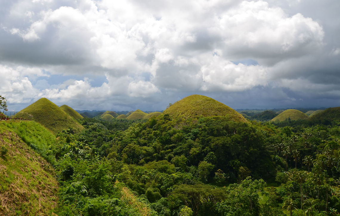 Chocolate Hills, Philippines Located in the island of Bohol, there are at least 1,260 dome-shaped limestone hills spread over an area of more than 50 square km, covered in green grass that turns brown (like chocolate) during the dry season, hence their name.<br />
These are conical karst hills similar to those seen in the limestone regions of Slovenia, Croatia, northern Puerto Rico, and Pinar del R&iacute;o Province, Cuba. They consist of Late Pliocene to Early Pleistocene, thin to medium bedded, sandy to rubbly marine limestones. These limestones contain abundant fossils of shallow marine foraminifera, coral, mollusks, and algae. The conical shape, called cockpit karst, was created by a combination of the dissolution of limestone by rainfall, surface water, and groundwater, and their subaerial erosion by rivers and streams after they had been uplifted above sea level and fractured by tectonic processes.  Fall,Geotagged,Philippines,bohol,chocolate hills,philippines,scenery