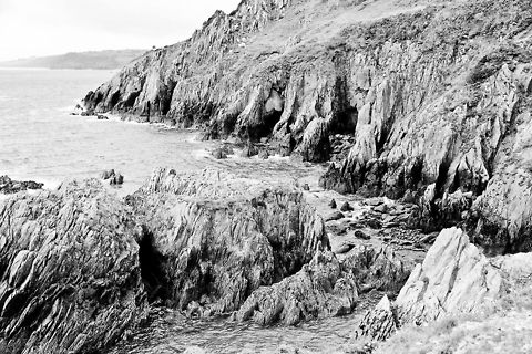Raw coastal enery I forced black and white with a lot of light on this photo to contrast the raw formation of rocks without disturbance of colour.  Wow, This Devon coastline is beautiful!
Taking this shot I actually (so Canon maintenance told me afterwards) got dust blown on my prisma right through the zoom tubes on my lens. The winds were extremely forceful on the height of rock I put my feet on (yet the sea seems quiet here). I did not even know it was possible. I suddenly noticed two  specs appear on my pentaprism. It spoiled my moment:) Geotagged,United Kingdom,coast,devon,formation,raw,rock,sea,wind