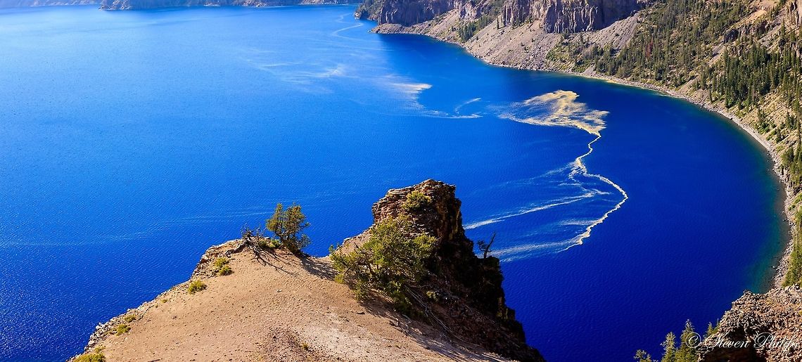 Pollen Trail The trail of yellow dust is actually pollen which is wind blown from surrounding pine trees that boarder the lake. A well-known crater lake, which bears the same name as the geological feature, is Crater Lake in Oregon. It is located in the caldera of Mount Mazama. It is the deepest lake in the United States with a depth of 594 m (1,949 ft). Crater Lake is fed solely by falling rain and snow, with no inflow or outflow at the surface, and hence is one of the clearest lakes in the world. blue water,caldera,crater lake,volcanic lake