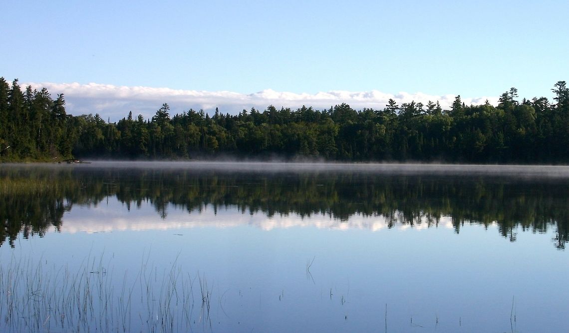 Astrid Lake in the early morning. Astrid Lake is a very clear lake about 57 acres in size with non-mineralized (soft) water. Surrounding forests are primarily a mixture of pines, spruce, fir, and aspen but pin oak and red maple are also common in places. The substrate is sand and gravel derived from regional gneiss bedrock. The lake is accessible by a footpath which continues past it into the pine forests on the other side. Astrid Lake,Geotagged,Minnesota,Summer,United States,early morning,lake,water
