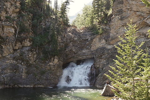Running Eagle Falls Montana The waterfall receives its nickname, "Trick Falls", because there are actually two separate waterfalls at this location. During the spring run-off, water rushes over the top ledge, creating a 40-foot drop, while completely or partially obscuring the lower falls. However, as the volume of water decreases by late summer, and the upper falls "dries up," water continues to rush through a sink hole at the top of the cliff before flowing out of an opening in the cliff face below, thus creating the lower 20-foot falls.

Towering prominently above the falls is 9513-foot Rising Wolf Mountain, which is named after the first white man to live with the Blackfeet Indians. Hugh Monroe, who was married to Sinopah, received his Indian name as a result of his habit of getting out of bed in the morning on his hands and knees, thus resembling a wolf. Rising Wolf Mountain also has the distinction of being the highest mountain in the Two Medicine area.

The waterfall is named for Pitamakan, or Running Eagle, a female warrior leader of the Blackfeet Nation in the early 1700s, who experienced a four-day vision quest in the mountains high above the falls. Running Eagle led war parties on many highly successful raids, and was the only woman in the Blackfeet tribe ever to do so, or to be given a man's name. Geotagged,Summer,United States