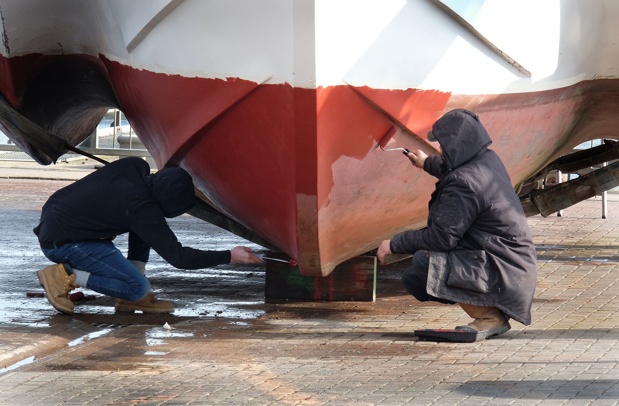 Men painting hull of a fishing boat out of the water. Two people painting a boat bottom