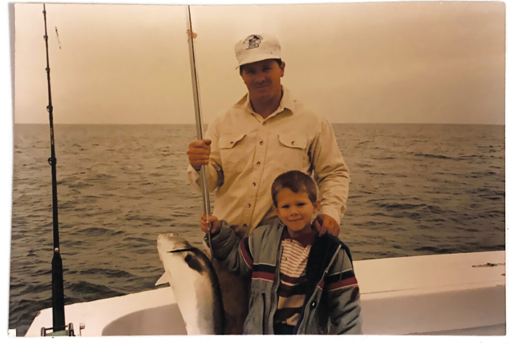 A man and a boy posing with a fish on a boat