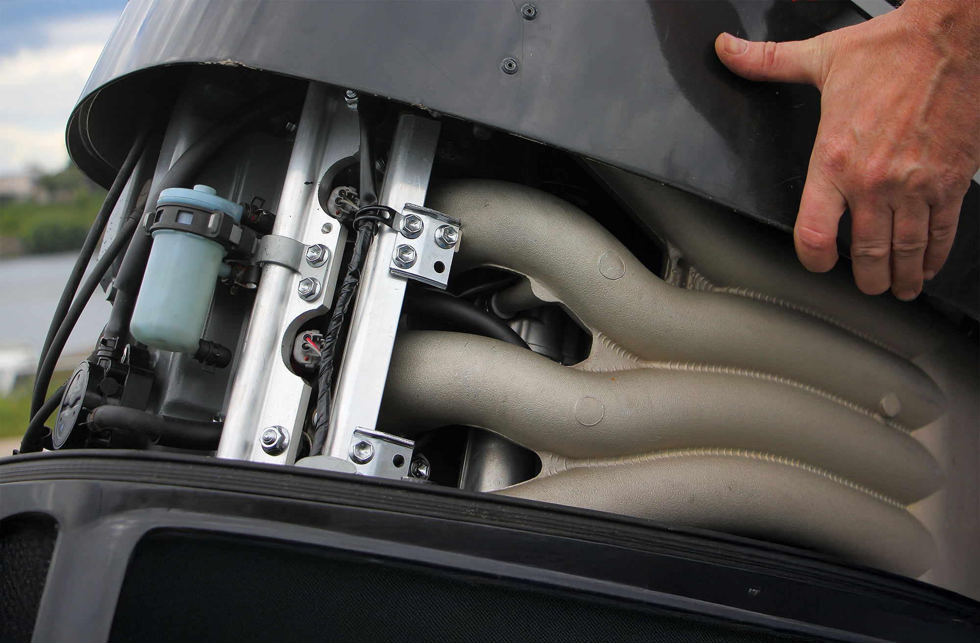 A man's hand open the hood of a powerful boat outboard motor