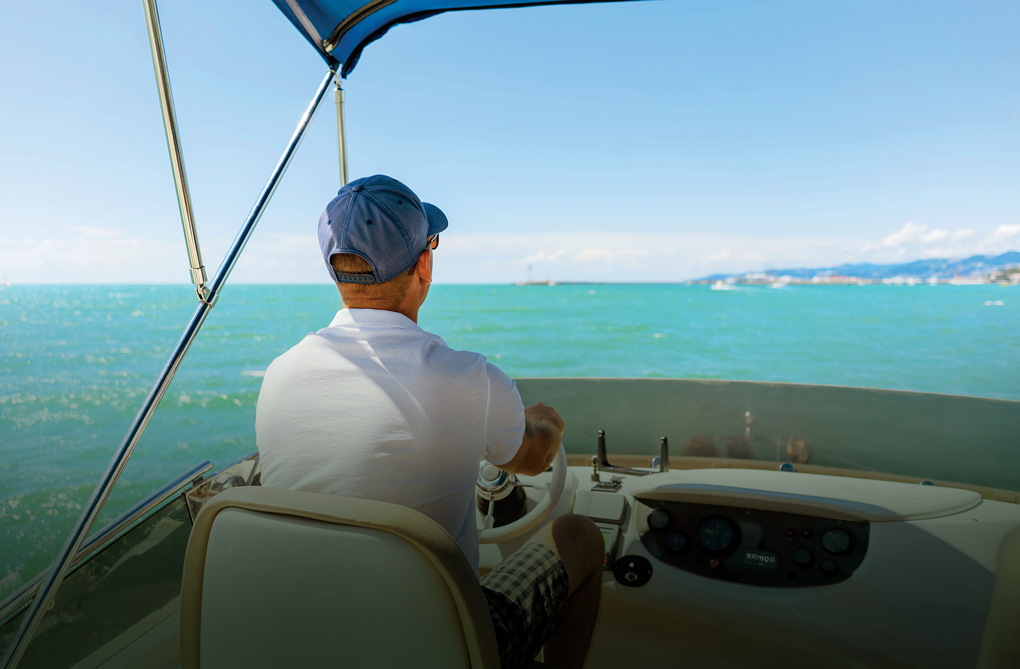 Man driving boat from a flybridge seen from behind.