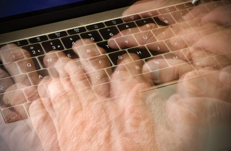 Caucasian mans hand typing on a laptop keyboard, blurred and showing movement