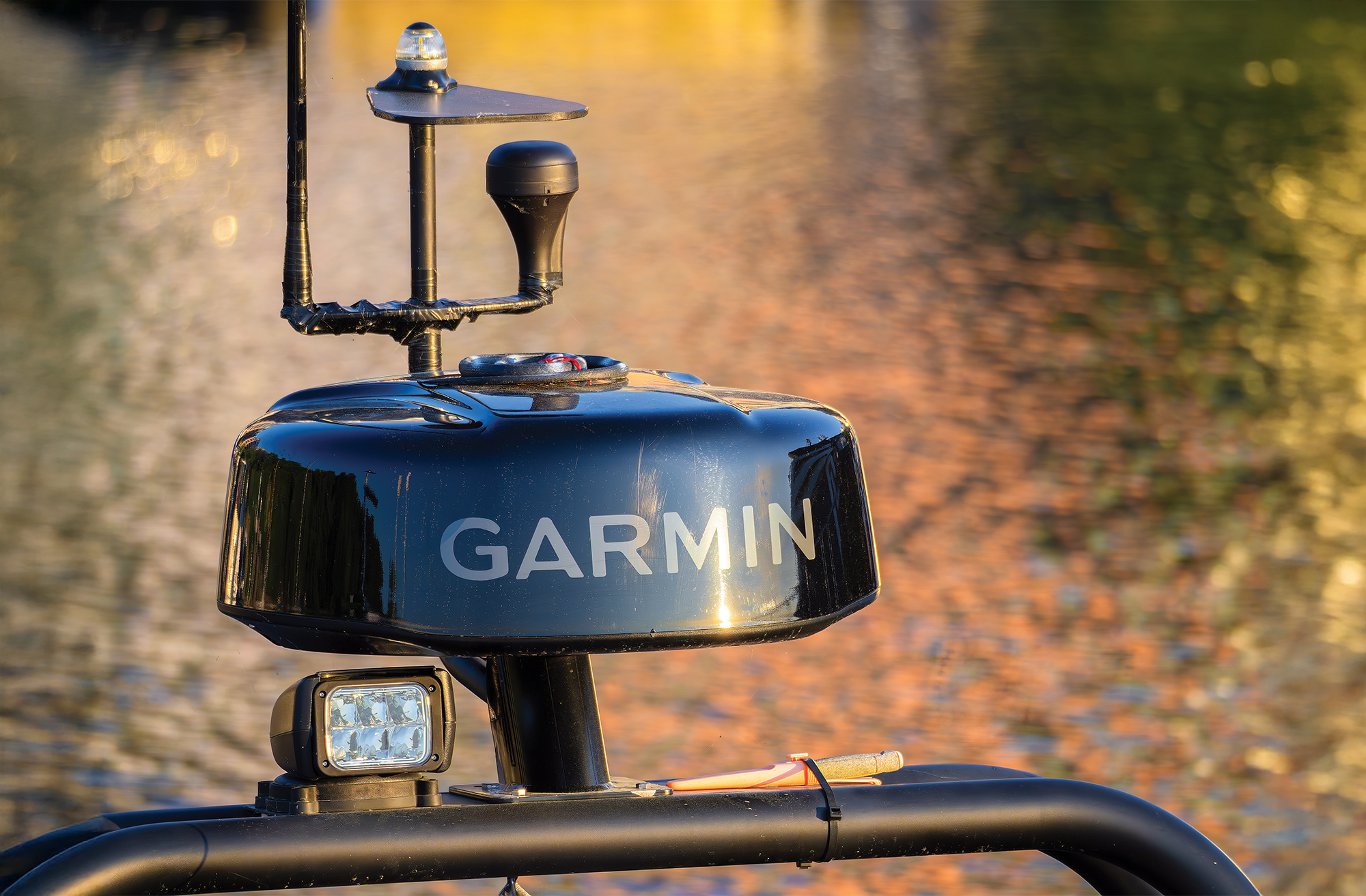 Close-up of a Garmin marine radar system mounted on a boat, with a blurred water background reflecting golden sunlight.