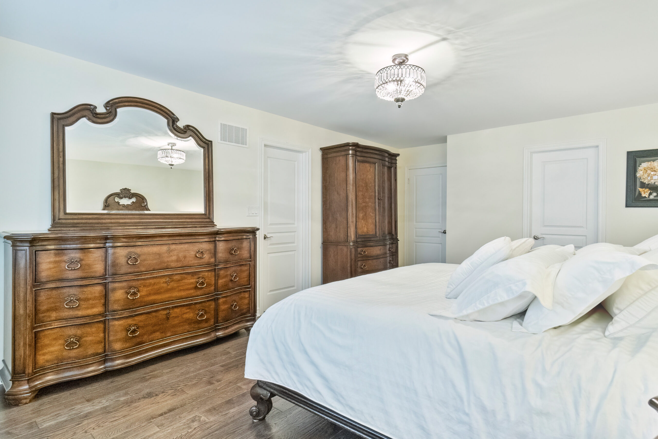 Cozy bedroom featuring a wooden dresser, a mirror, and a bed with white linens