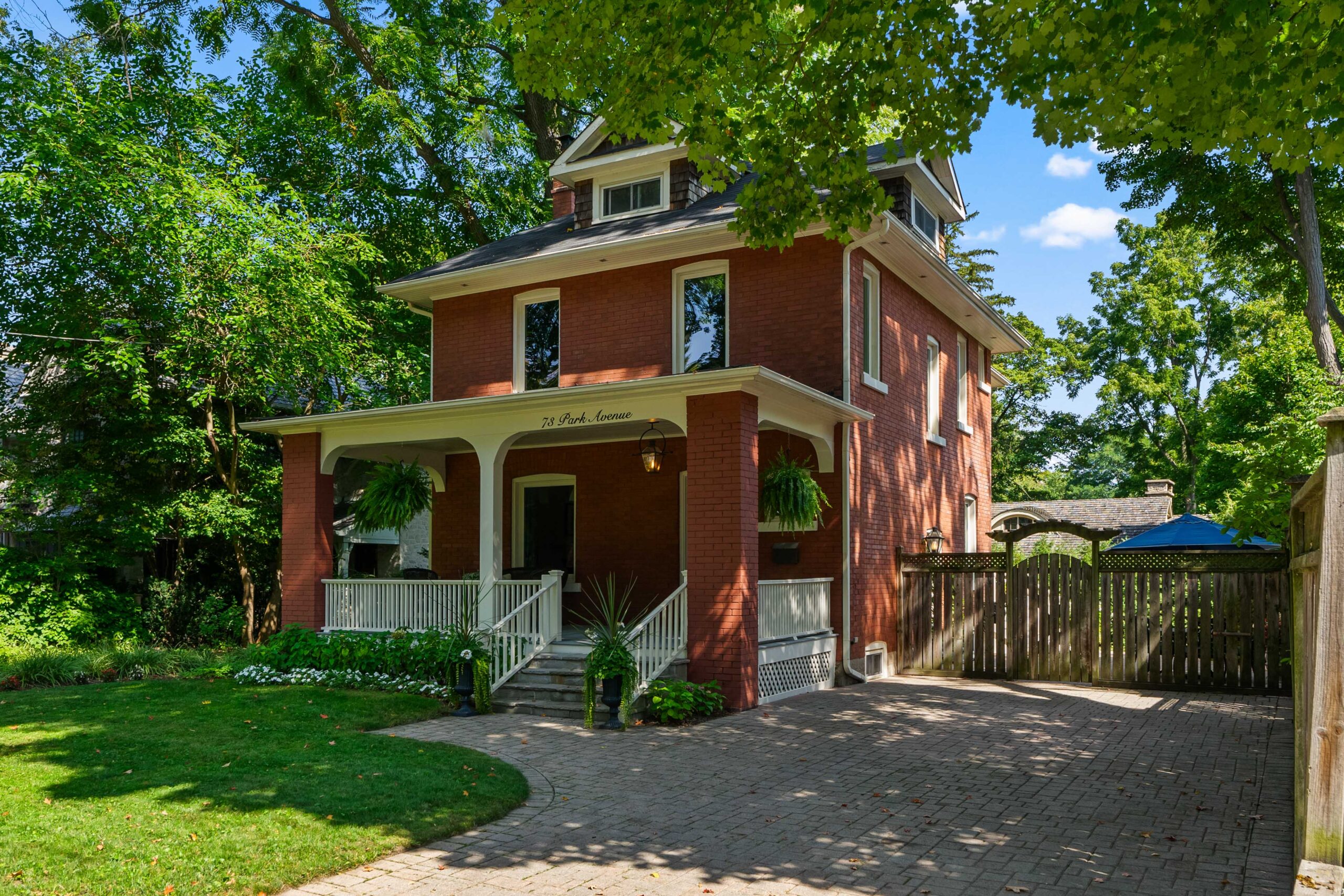 Victorian-style red brick house surrounded by greenery and a paved driveway