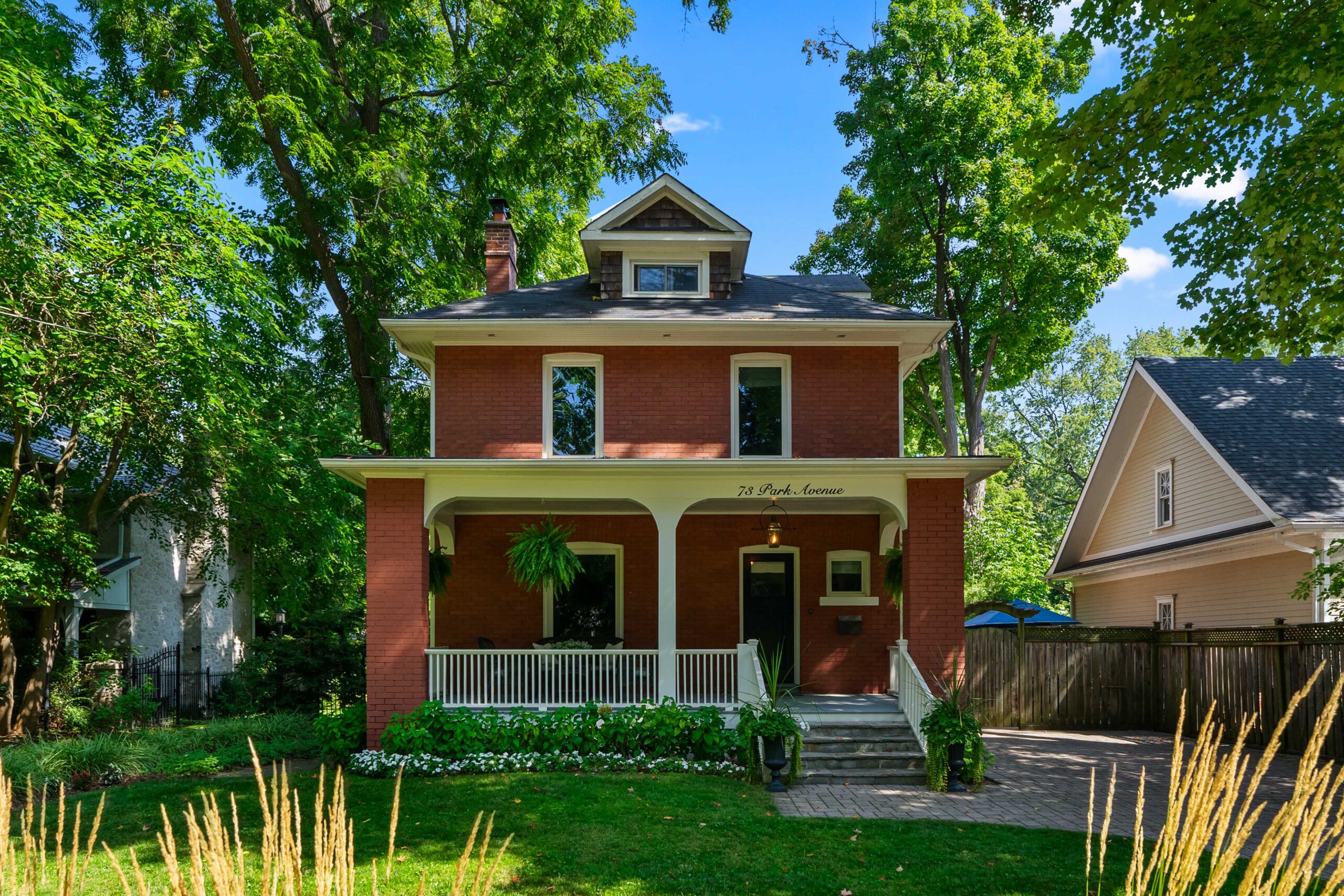 Two-story red brick house surrounded by lush greenery and trees