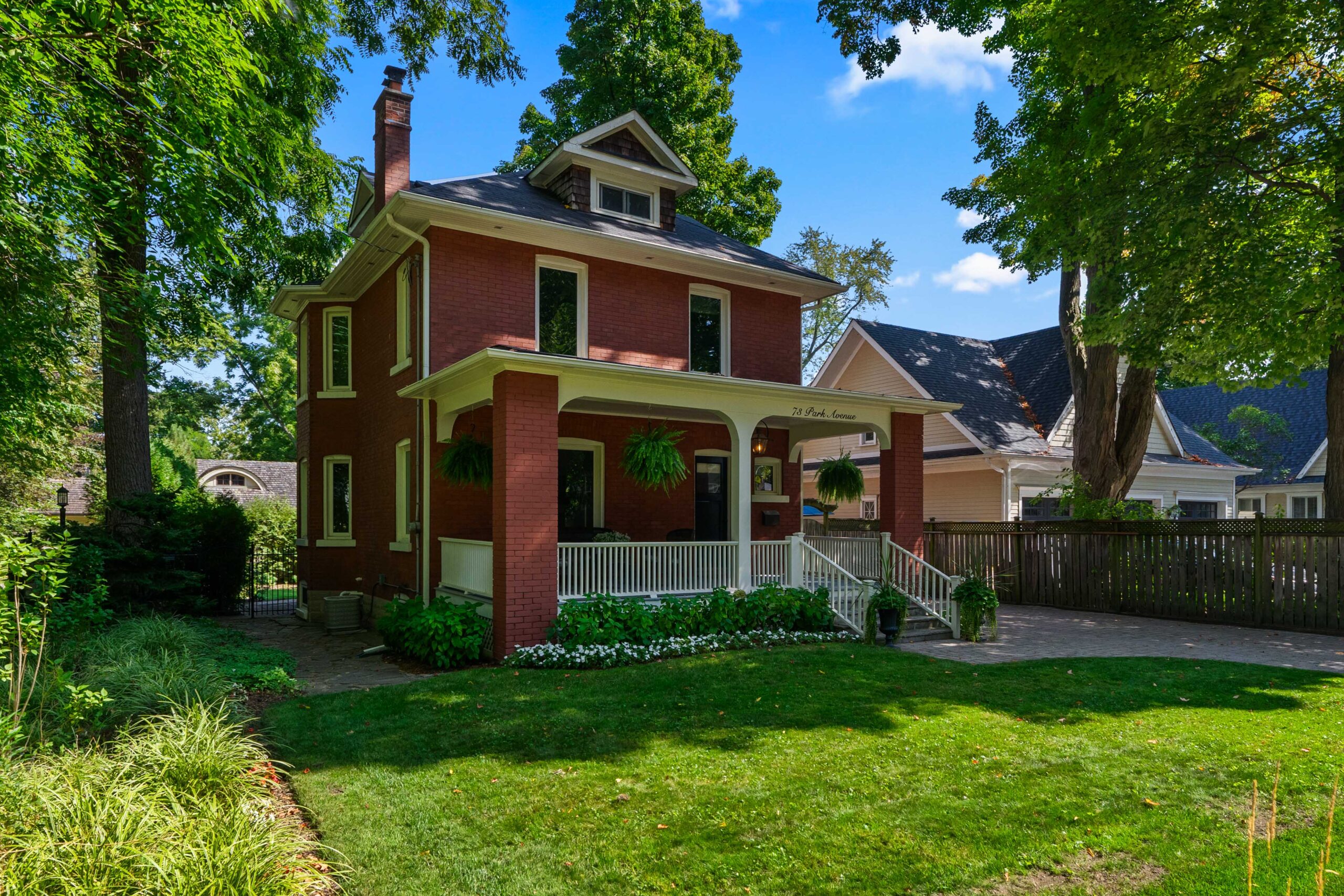 Red brick house with a porch surrounded by green trees and lawn